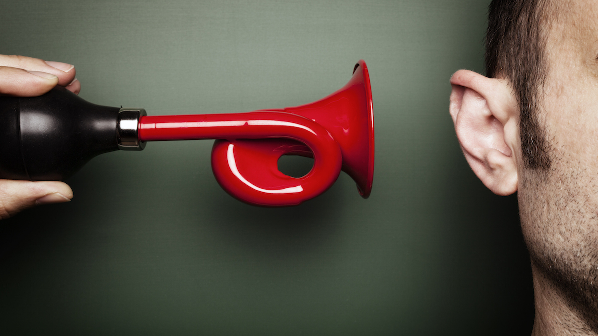 Conceptual photography. Somebody's holding a red signal horn very close to an ear.