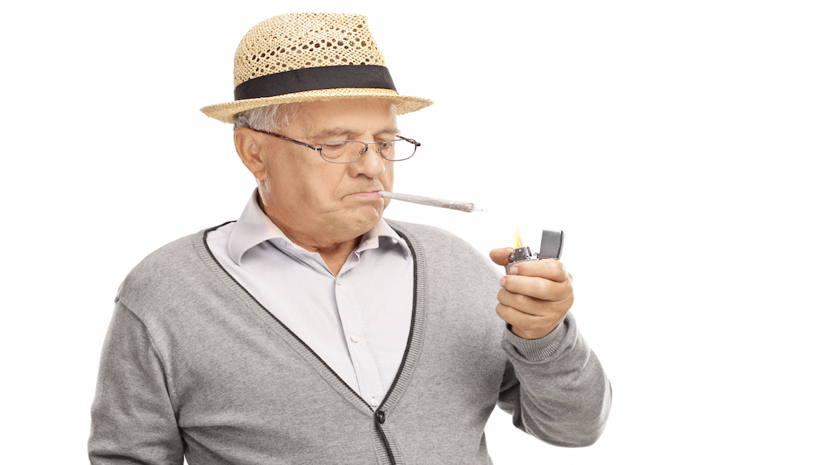 Senior man lighting up a joint with a gray lighter isolated on white background