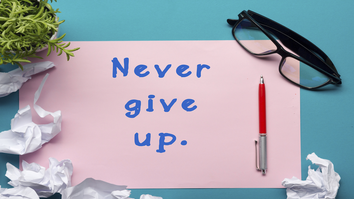 Never give up message - Office desk table with supplies top view.  crumled paper, pen, glasses and flower